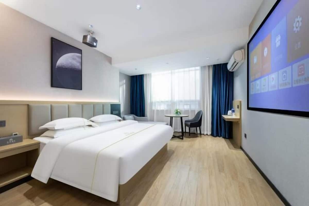 A hotel room with a bed, a desk, a chair, a TV, and a window with curtains.