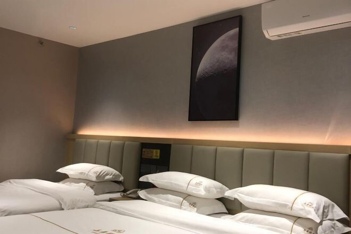 A hotel room with a bed, pillows, a headboard, and a wall-mounted air conditioner.