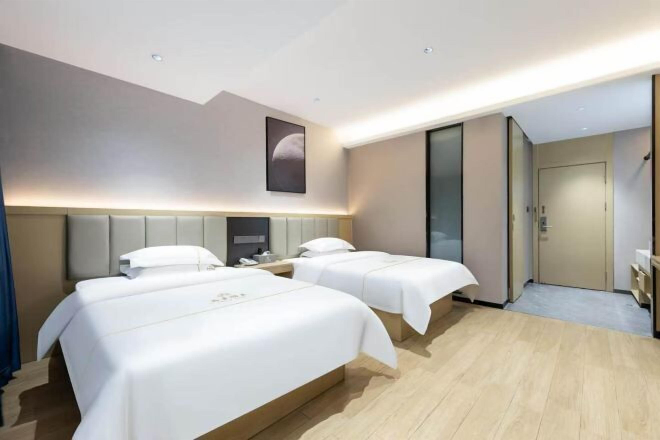 Habitación de hotel con dos camas, un espejo grande, un armario y una puerta que da al baño.