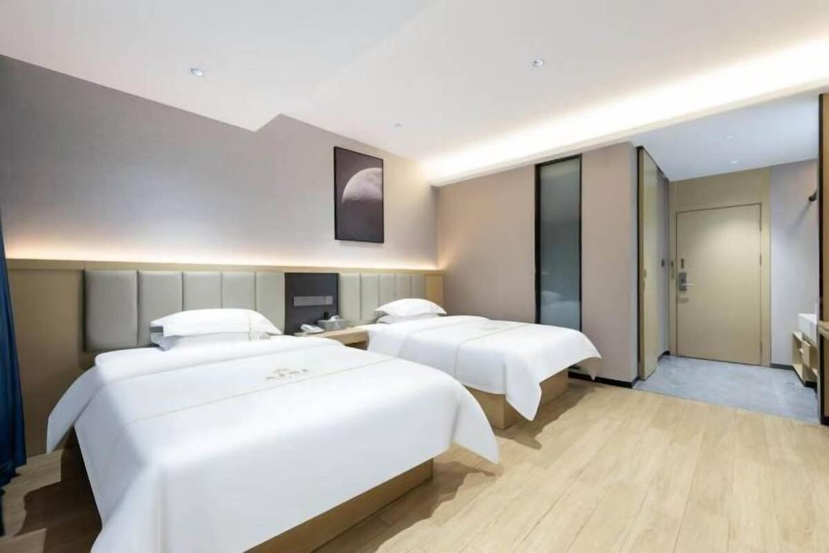 A hotel room with two beds, a large mirror, a wardrobe, and a door leading to a bathroom.