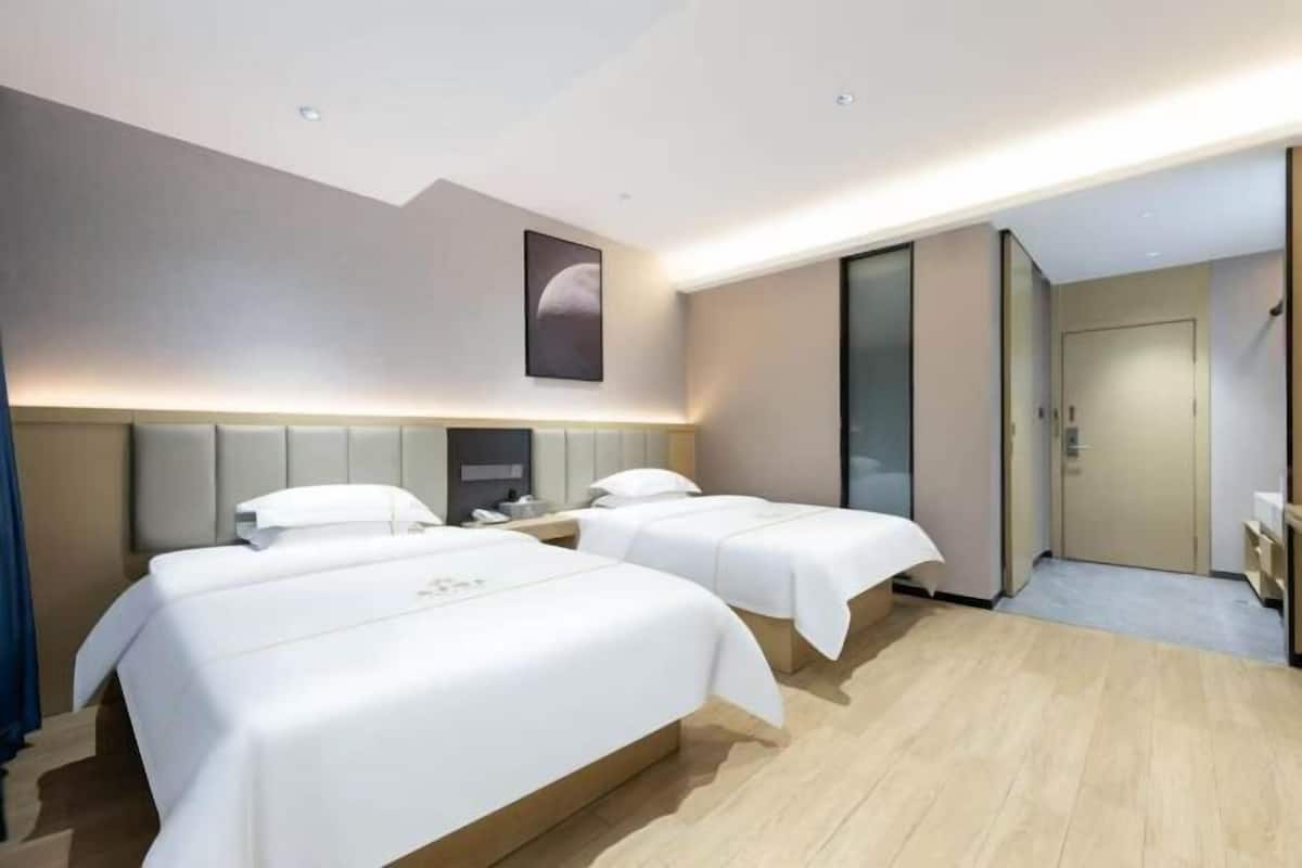 A hotel room with two beds, a large mirror, a wardrobe, and a door leading to a bathroom.