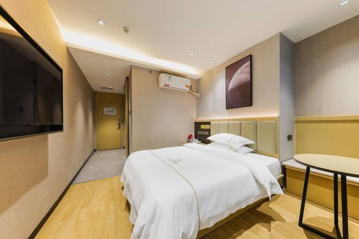 A hotel room with a bed, bedside table, and a mounted TV.