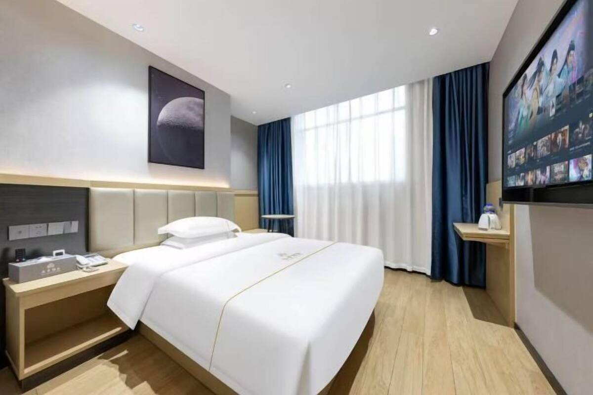 A hotel room with a bed, bedside table, TV, and curtains.
