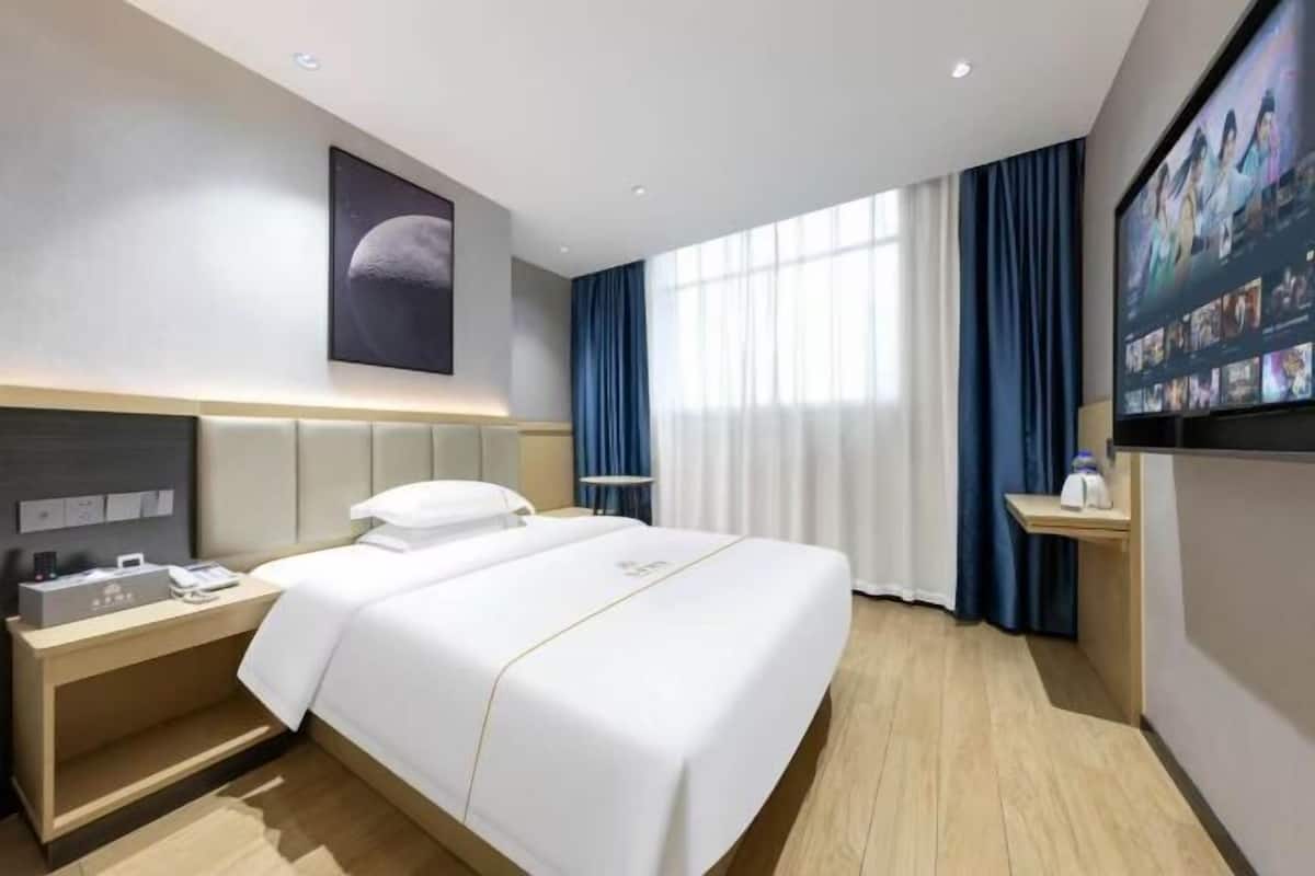 A hotel room with a bed, bedside table, TV, and curtains.