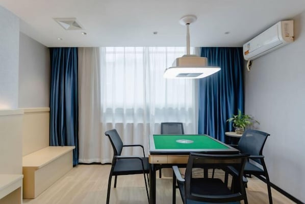 A room with a green pool table, black chairs, a bench, a hanging light fixture, and a window with blue curtains. - Jiahua Hotel (Guangzhou Xintang) (Guangzhou)