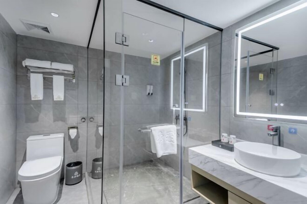 A modern bathroom with a glass shower enclosure, a toilet, a sink with a large mirror, and a towel rack.
