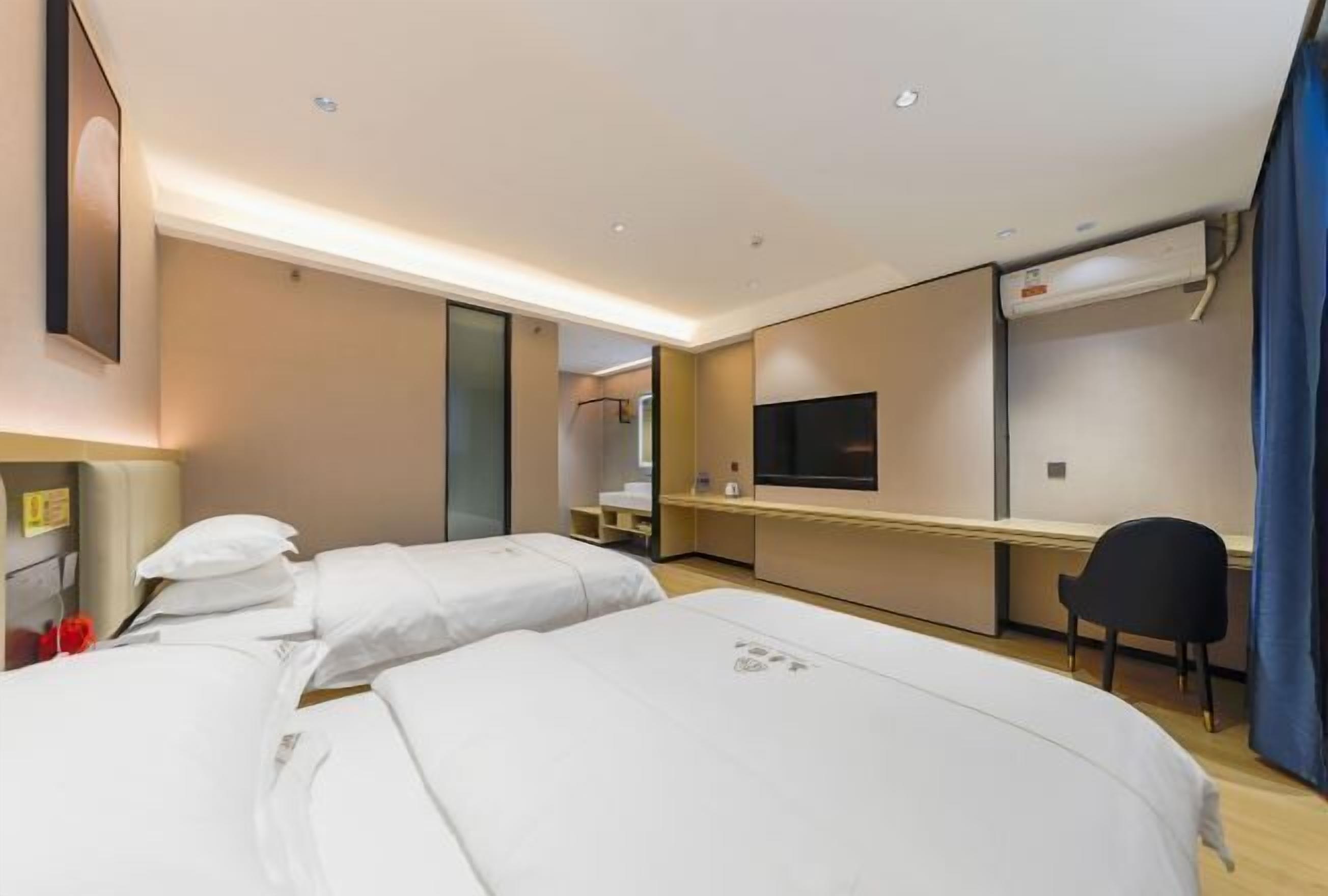 Habitación de hotel con dos camas, un escritorio, una silla, un televisor y una ventana con cortinas.