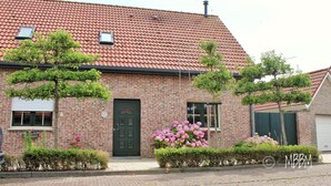 Ein Backsteinhaus mit grüner Tür, einem Fenster mit Fensterläden und einem kleinen Baum davor.