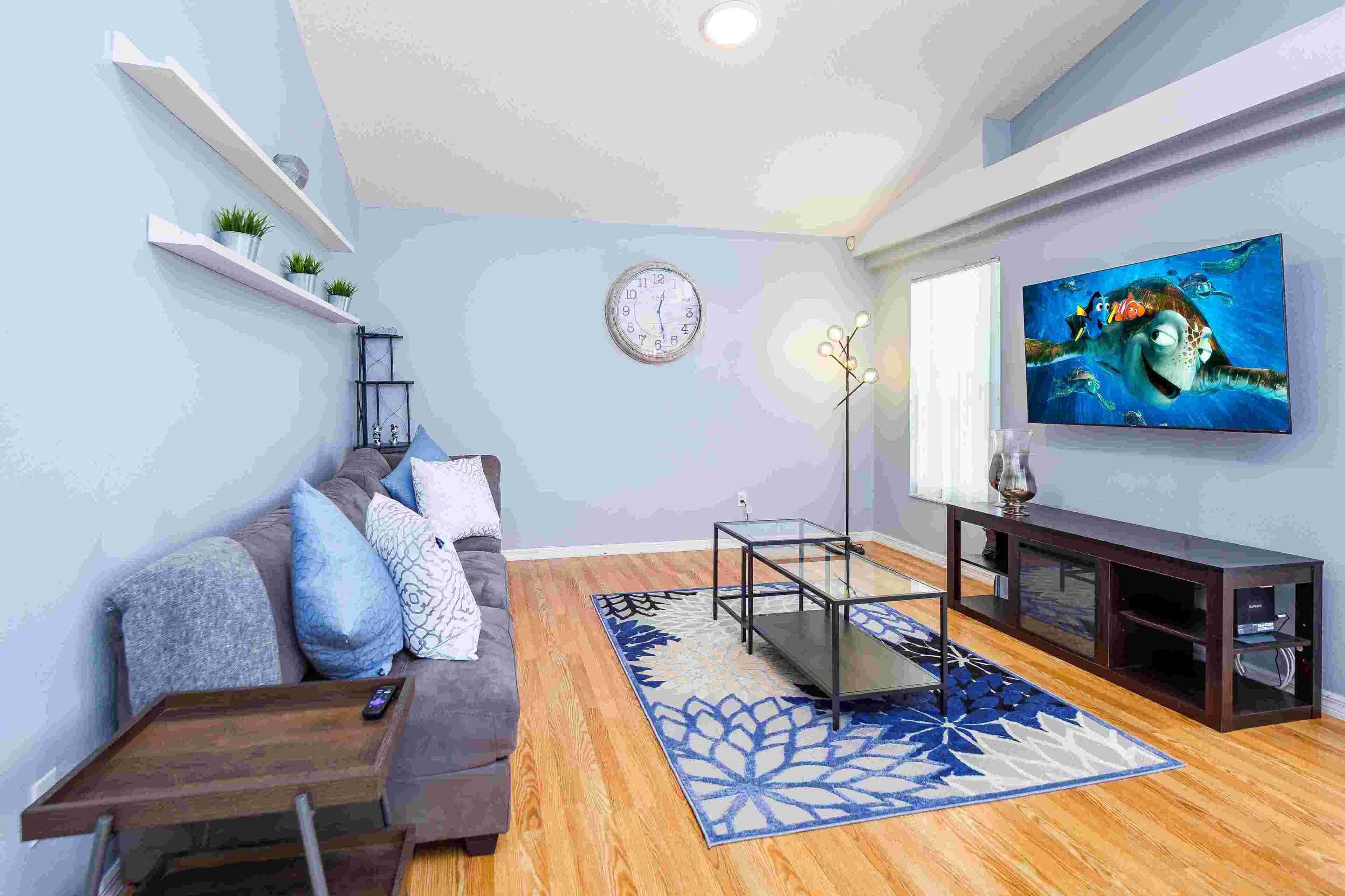 A living room with a sofa, coffee table, TV, shelves, and a clock.