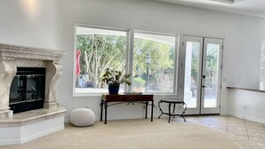 A spacious living room with a fireplace, large windows, and a view of greenery outside. - Southshore single story Tuscany style home for rent! (Henderson)