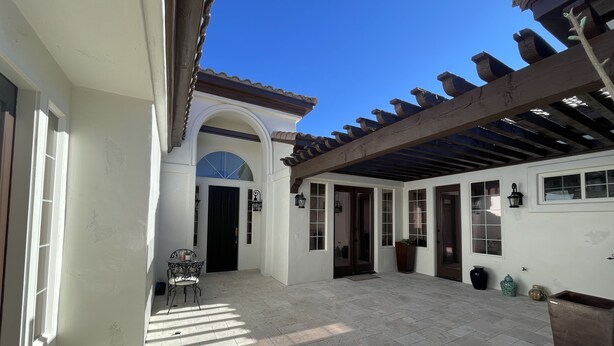 A covered patio area with tiled flooring, a black door, and a pergola structure. - Southshore single story Tuscany style home for rent! (Henderson)