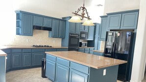 A kitchen with blue cabinets, a granite countertop, stainless steel appliances, and a hanging light fixture. - Southshore single story Tuscany style home for rent! (Henderson)