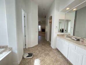 A bathroom with a large mirror, white cabinets, and a scale on the floor.