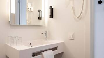A modern bathroom with a white sink, a mirror, a towel rack, and a hairdryer mounted on the wall.