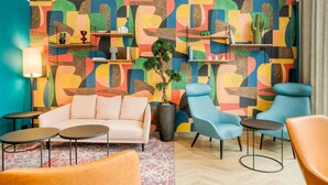 Un salon moderne avec un mur décoré d’une œuvre abstraite aux couleurs vives, un canapé blanc, des fauteuils bleus et une petite table basse.