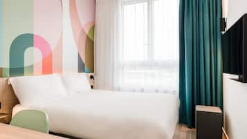 A hotel room with a bed, a desk, a chair, a TV, and a window with curtains.