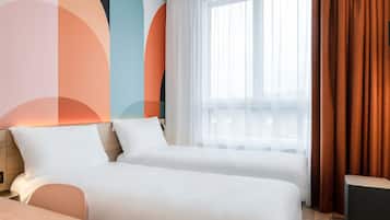 A hotel room with two beds, a wooden headboard, a window with sheer curtains, and a view of the city.