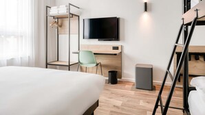 Une chambre d’hôtel comprenant un lit, un bureau avec une chaise, une télévision, une armoire et une échelle.