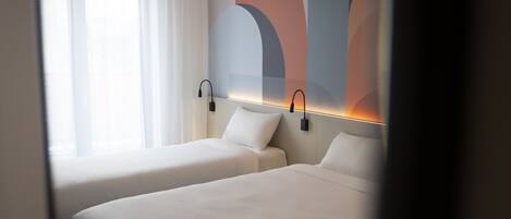 Habitación de hotel con dos camas, un ventanal con cortinas blancas y una pared decorada con arte abstracto.