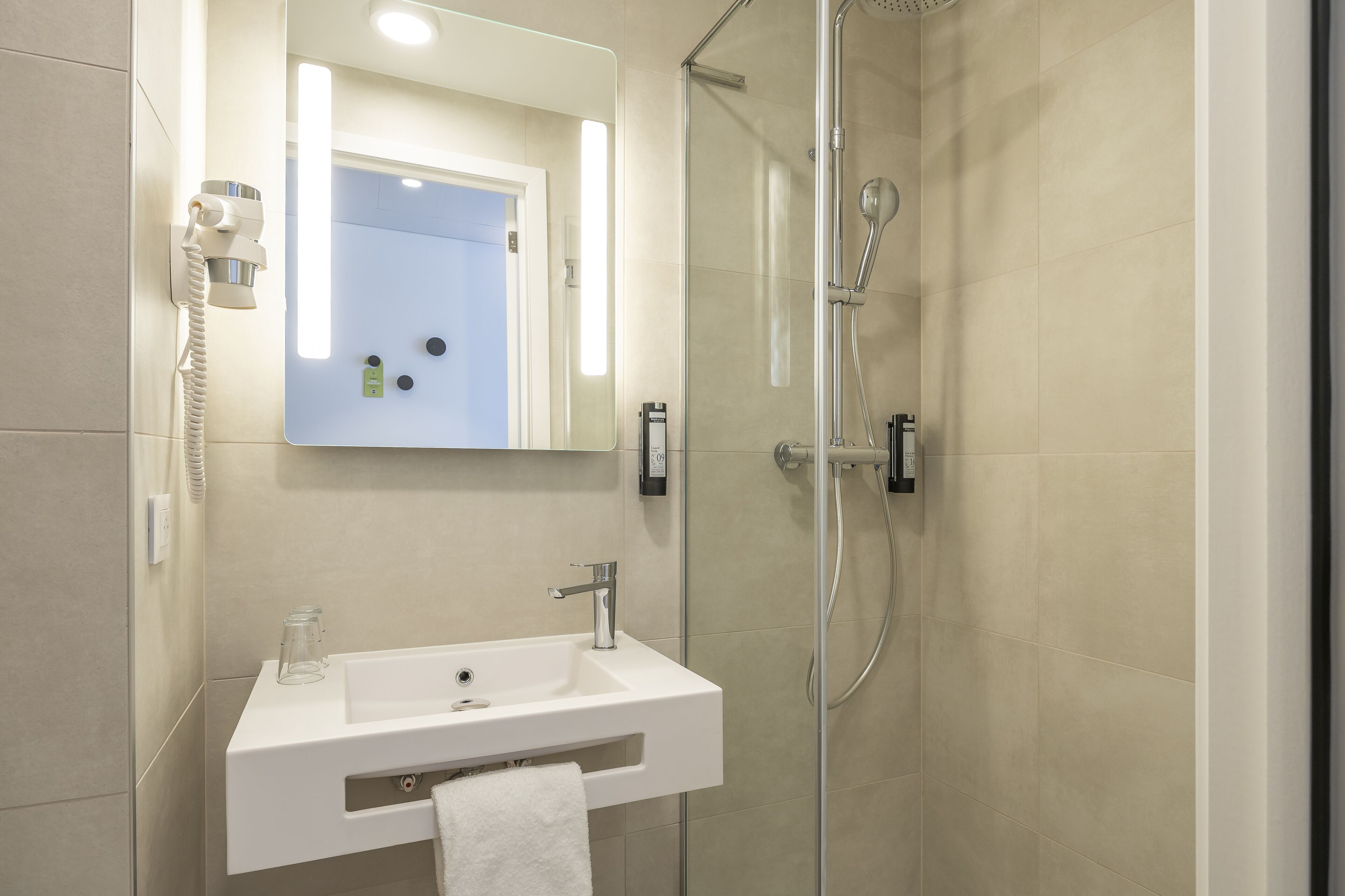 A modern bathroom with a glass-enclosed shower, a white sink, and a mirror with integrated lighting.