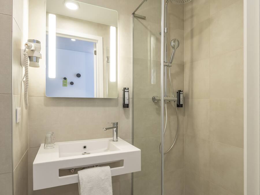 Un baño moderno con ducha envuelta en vidrio, un lavabo blanco e iluminación integrada en un espejo.