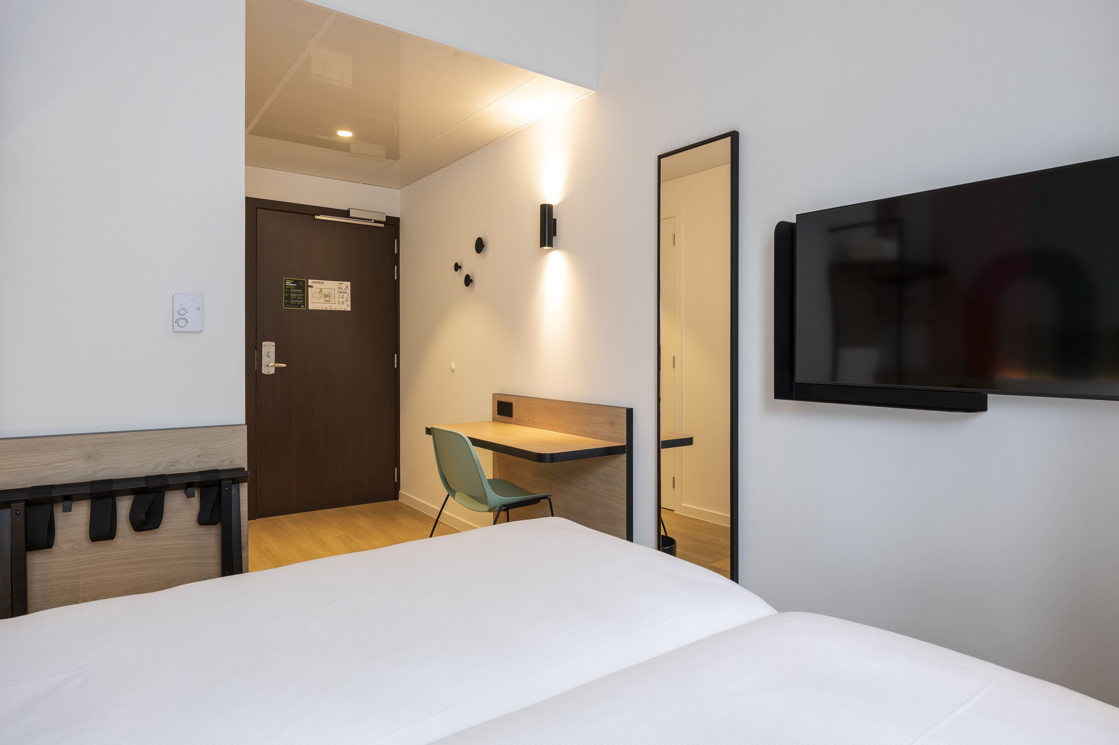 Une chambre d’hôtel comprenant un lit, un bureau, une chaise, un téléviseur fixé au mur et une porte donnant sur une autre pièce.