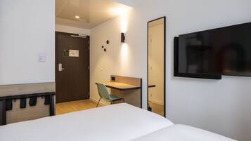 Une chambre d’hôtel comprenant un lit, un bureau, une chaise, un téléviseur fixé au mur et une porte donnant sur une autre pièce.