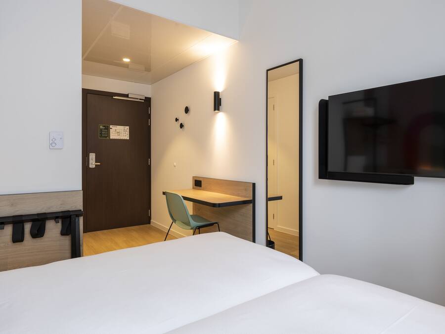 Une chambre d’hôtel comprenant un lit, un bureau, une chaise, un téléviseur fixé au mur et une porte donnant sur une autre pièce.