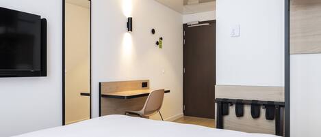 Una habitación de hotel moderna con cama, escritorio, silla, televisor y armario.