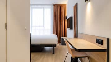 A hotel room with a bed, a desk, a chair, a TV, and a window with curtains.