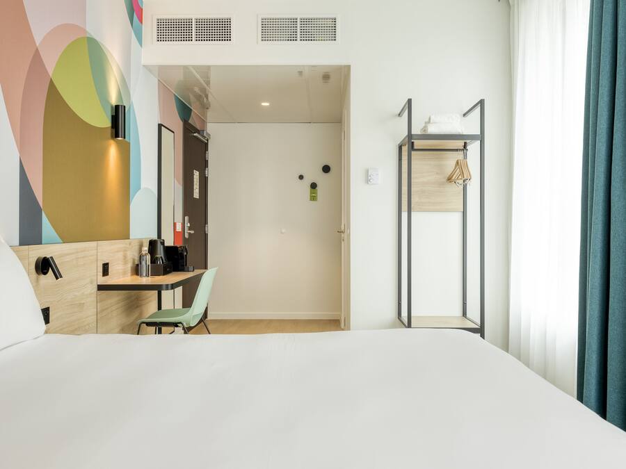 A hotel room with a bed, a desk, a chair, a wardrobe, and a bathroom door.