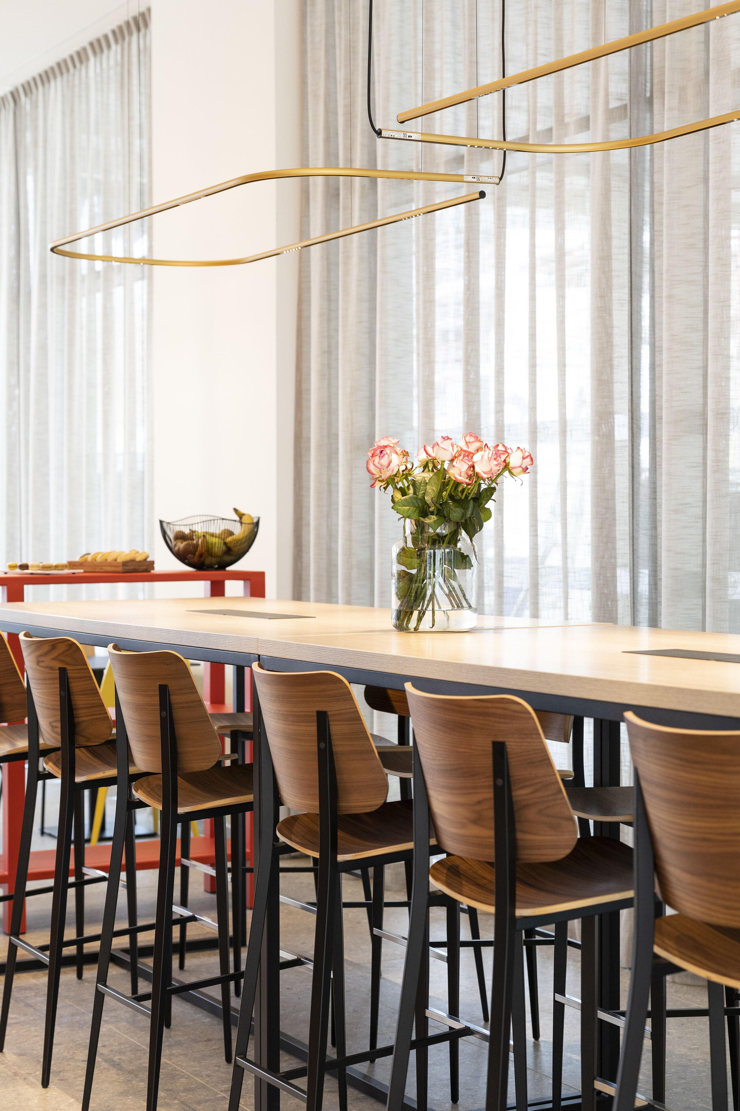 Un coin repas avec une longue table, des chaises, un vase rempli de fleurs et un saladier posé sur la table.