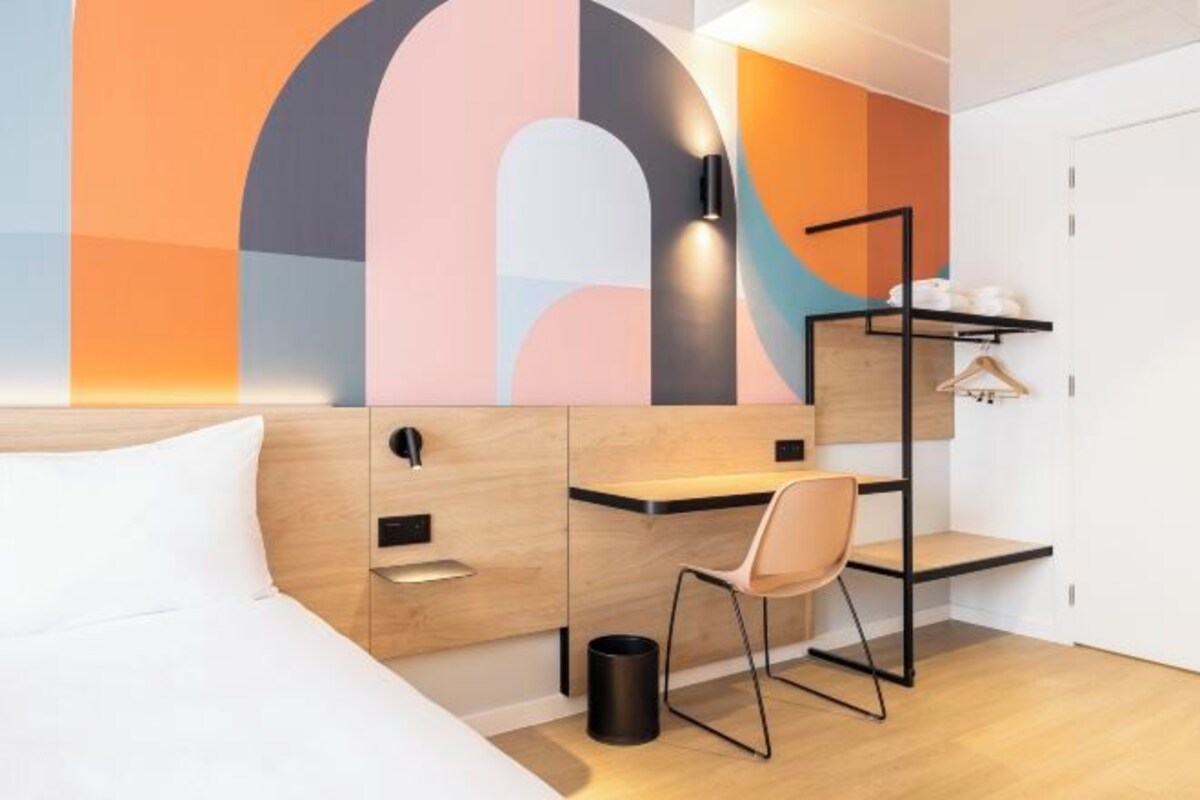 Una habitación de hotel moderna con una cama, un escritorio, una silla y un armario.