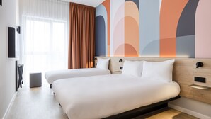 Habitación de hotel con dos camas, un ventanal con cortinas, una pared con arte abstracto y un cabecero de madera.