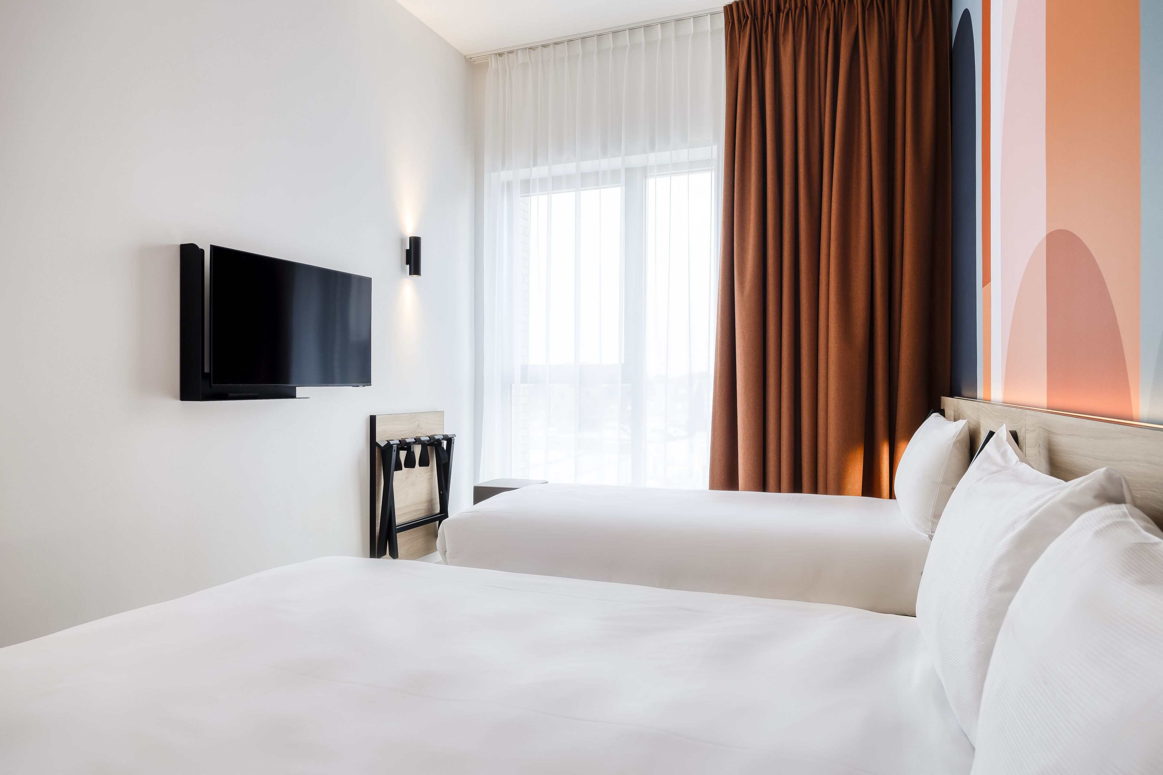 A hotel room with a bed, a TV mounted on the wall, and a window with curtains.