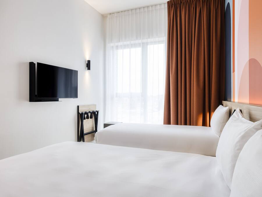 A hotel room with a bed, a TV mounted on the wall, and a window with curtains.