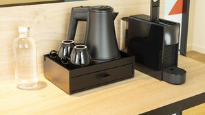 Un escritorio de madera con una cafetera, un hervidor, una botella y un portavasos.