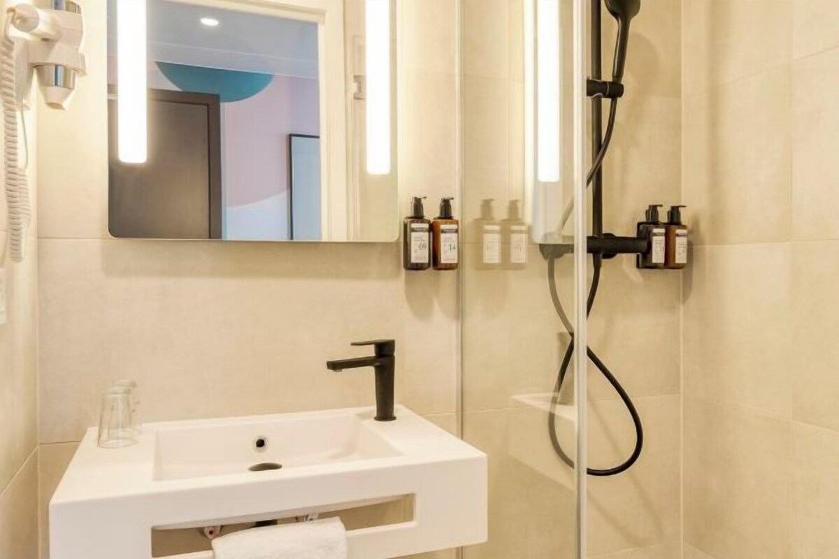 Un baño moderno con un lavamanos blanco, un cabezal de ducha de mano y un espejo sobre el lavamanos.