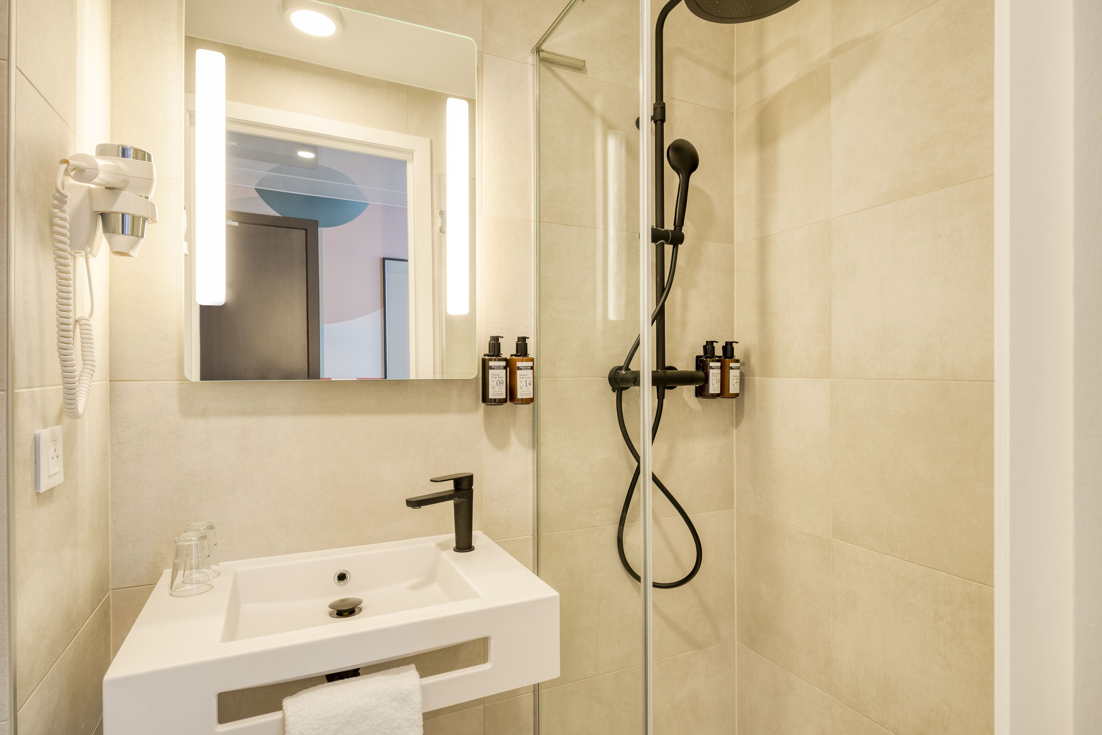 A modern bathroom with a white sink, a handheld showerhead, and a hairdryer mounted on the wall.