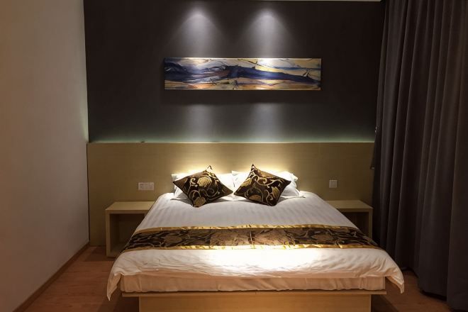 A bedroom with a bed, two bedside tables, a headboard, and a wall-mounted artwork.