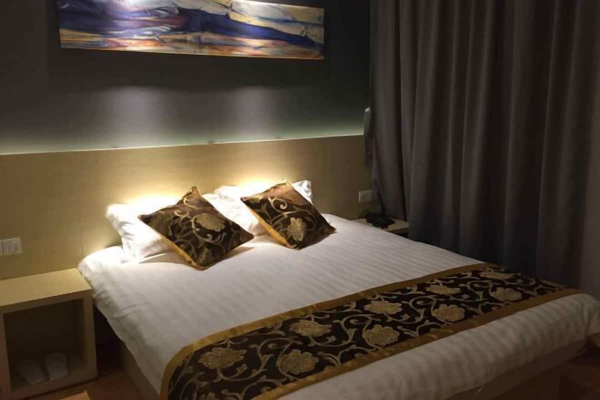 Habitación de hotel con cama, almohadas, cabecera, mesita de noche y un cuadro en la pared.