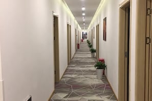 Um longo corredor com portas em ambos os lados, plantas em vasos e um chão com padrão.