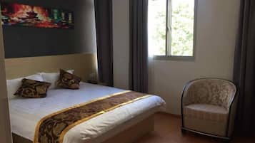 A neatly made bed with a patterned bedspread, a chair, and a window with curtains.