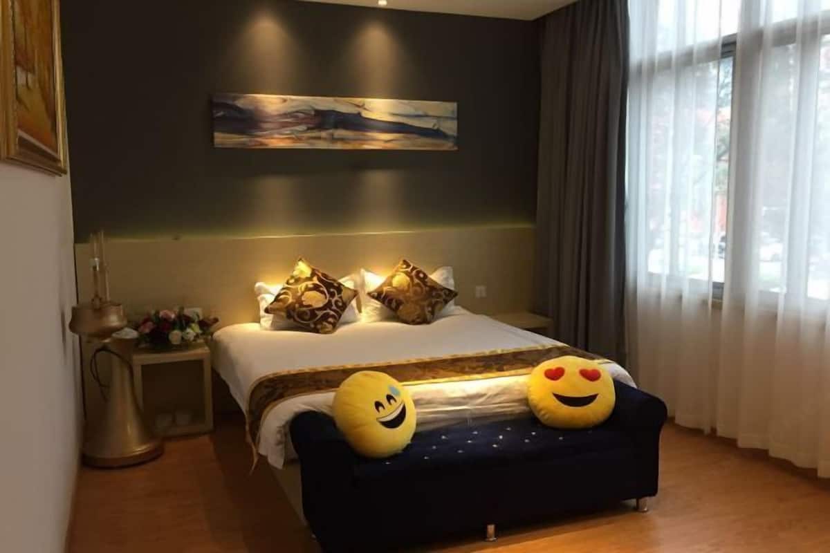 Un dormitorio con cama, almohadas, una mesita de noche con lámpara y una ventana con cortinas.