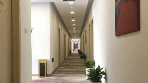 A hotel corridor with a geometric patterned floor, doors on both sides, and potted plants. - Juzi Select Hotel (Shanghai)