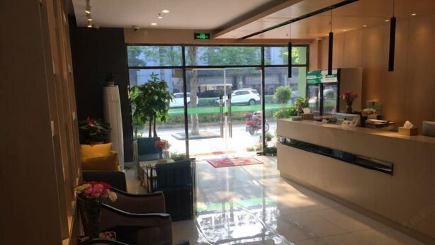 A hotel reception area with a glass door leading outside, a reception desk, and seating area with chairs and a table. - Juzi Select Hotel (Shanghai)