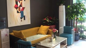 A modern room with a yellow sofa, a white coffee table, and a blue chair. There is a large window with plants outside. - Juzi Select Hotel (Shanghai)