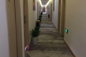 A hallway with a tiled floor, potted plants, and a light switch on the wall. - Juzi Select Hotel (Shanghai)