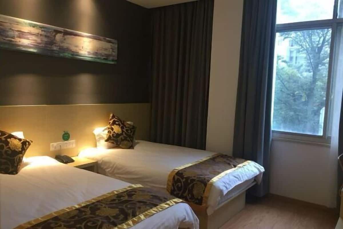 Habitación de hotel con dos camas, una mesita de noche con teléfono, un cuadro en la pared y una ventana con cortinas.