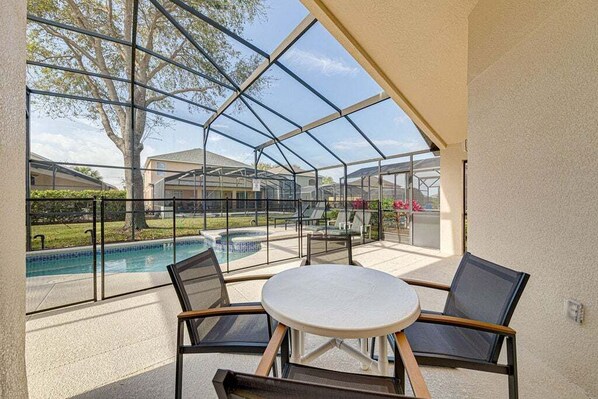 A covered outdoor seating area with a pool view, glass walls, and a table and chairs.